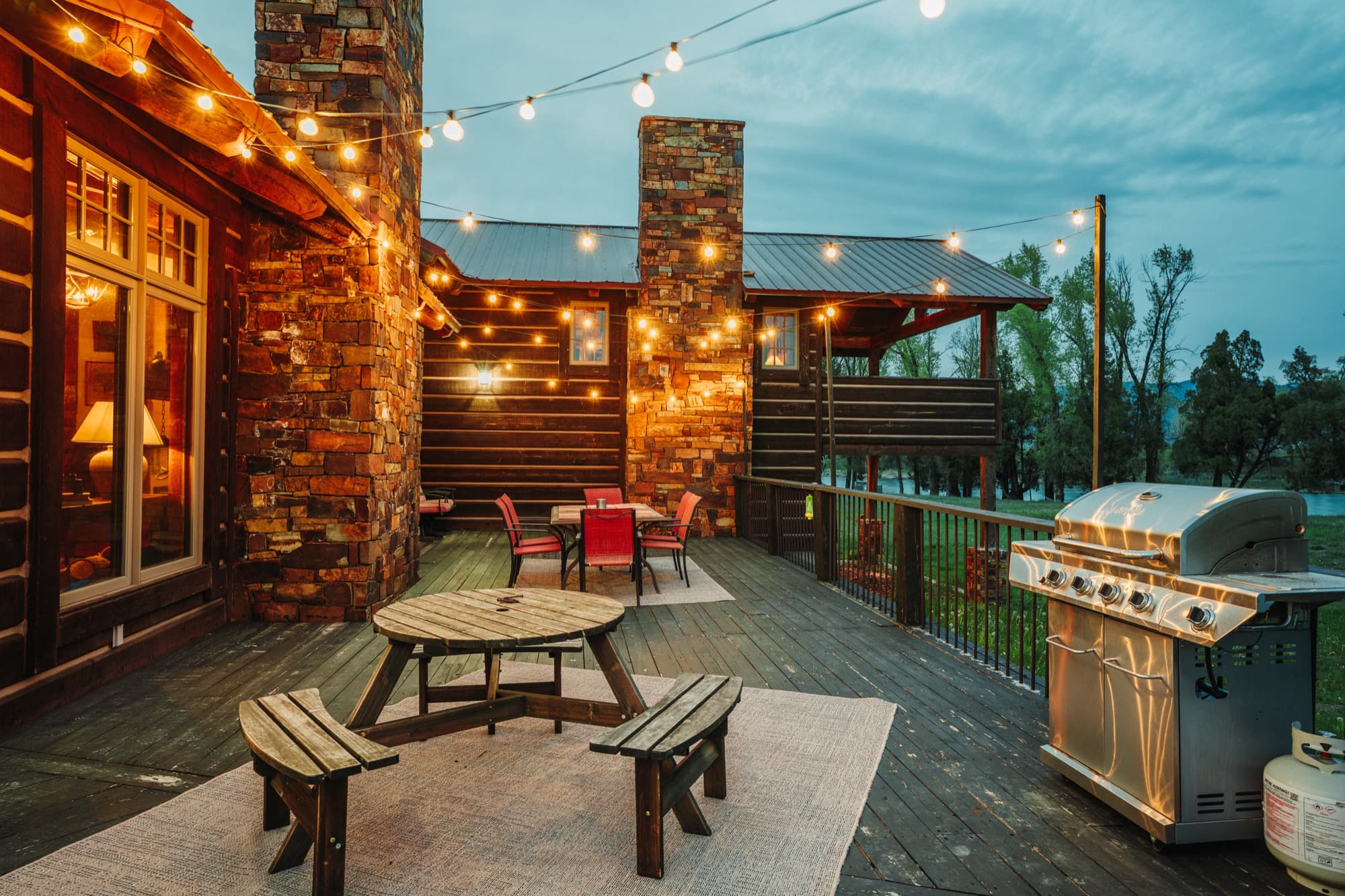 Deck with picnic-table dining and gas grill under string lights at dusk