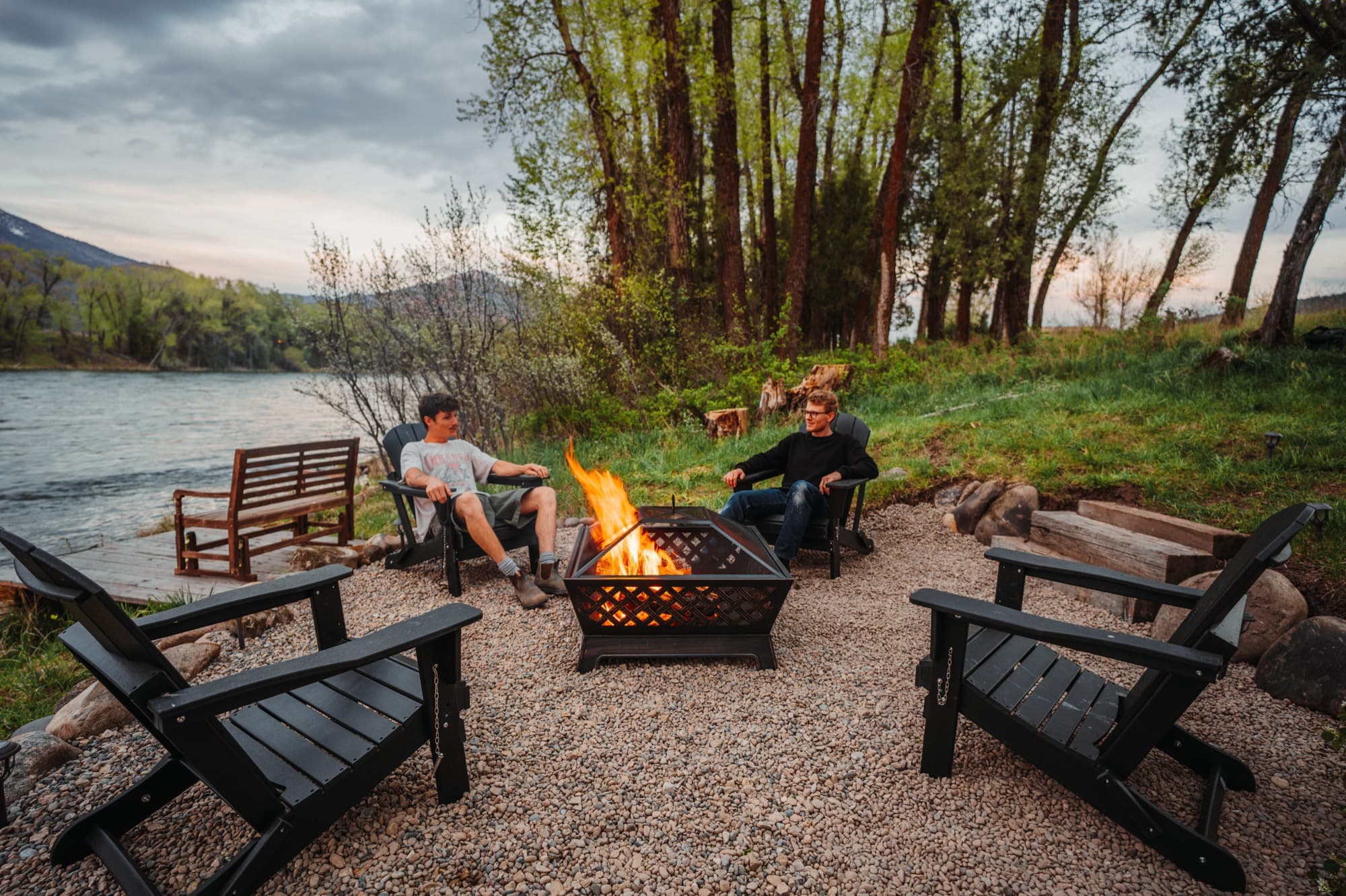 Guests and their dog relaxing around a lit firepit beside the Snake River