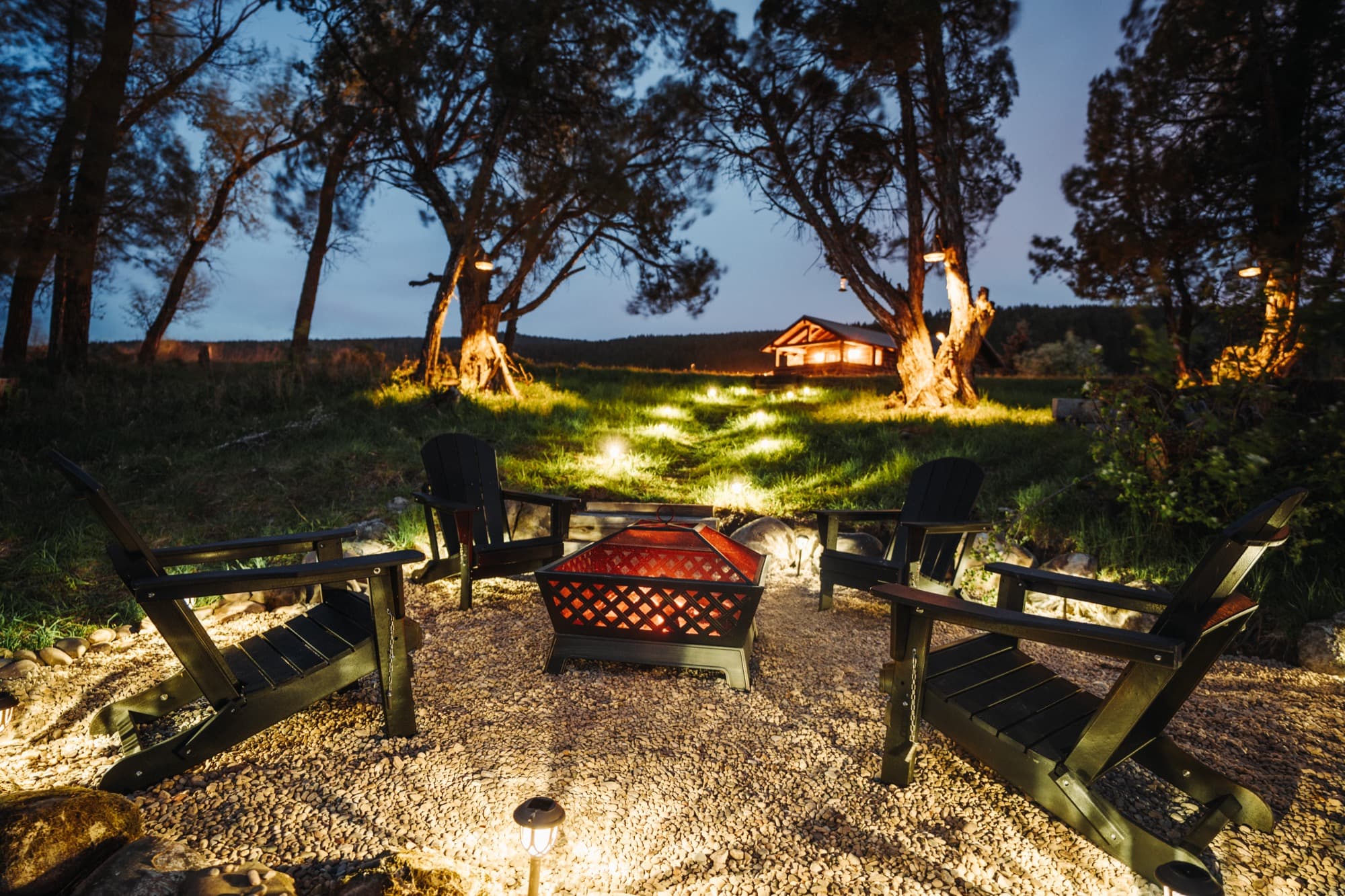Firepit glowing at night with landscape lighting under the trees
