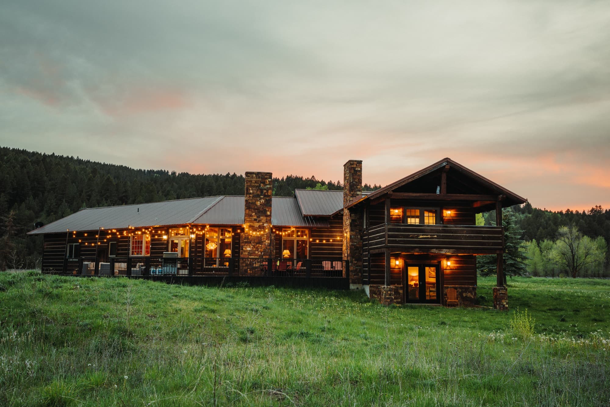 Log cabin exterior at sunset with lit windows and string lights, Swan Valley, Idaho